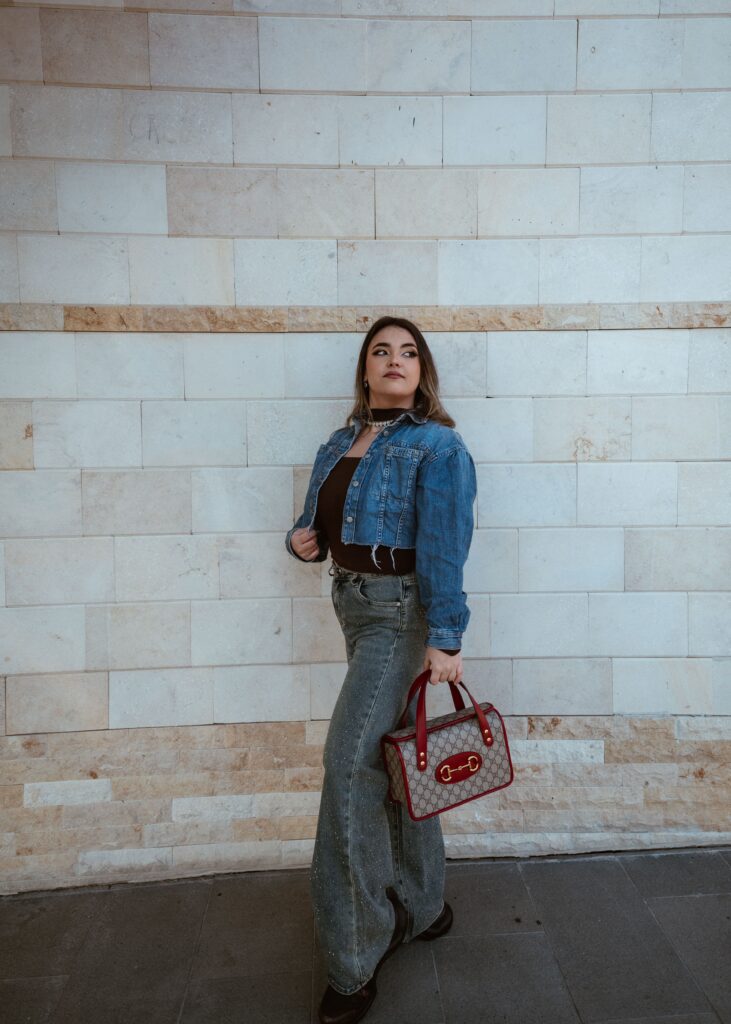 Woman carrying a red-trimmed Gucci monogram handbag with a denim outfit