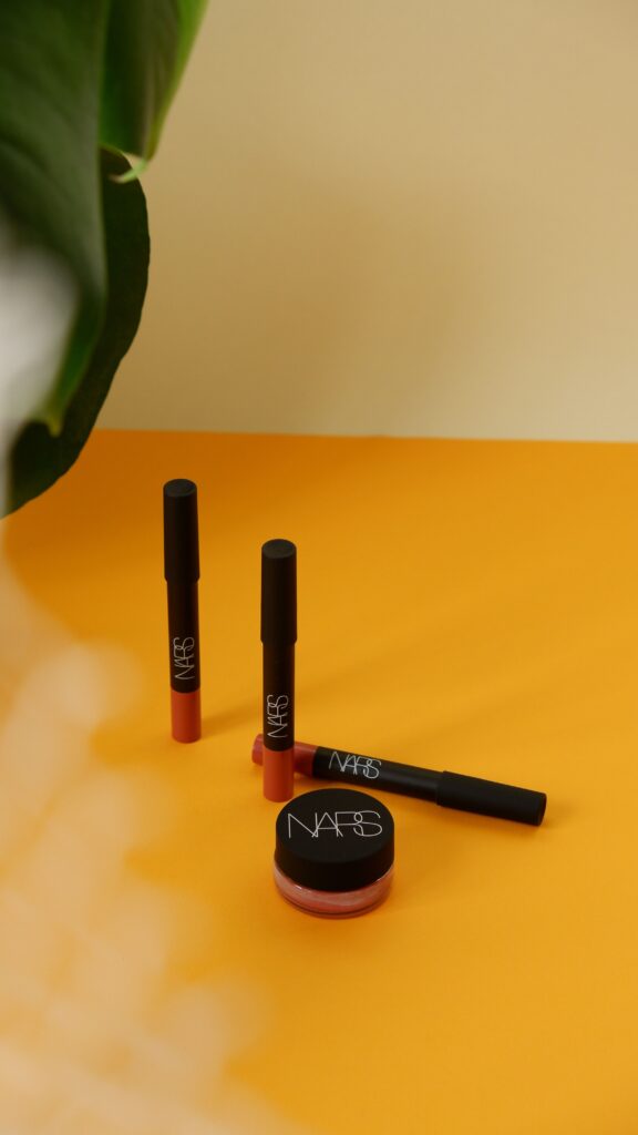 NARS lip products and a branded cosmetic pot on a yellow surface