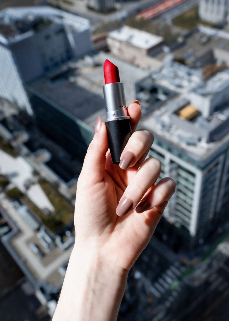 Hand holding a red MAC lipstick above a city background