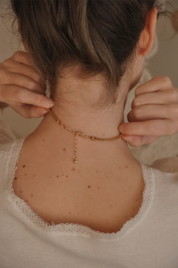 Hands fastening a delicate necklace at the back of a neck