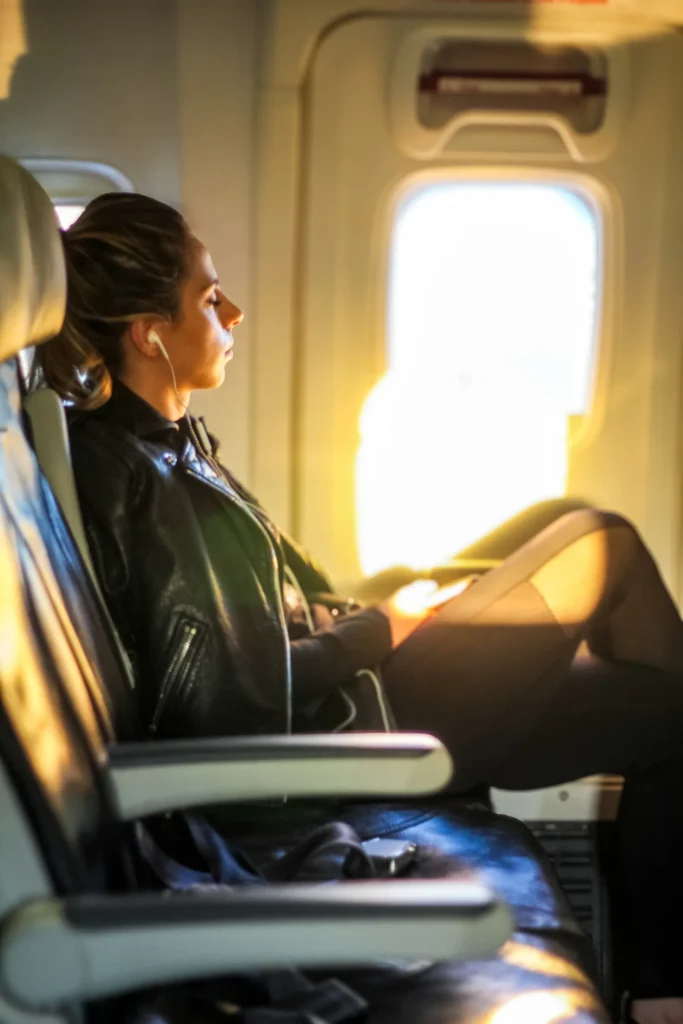 An aircraft passenger wearing wired earphones beside a window