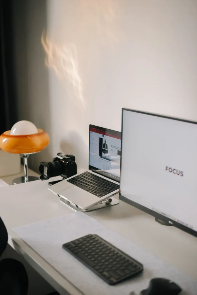 A desk with monitor, laptop, keyboard and task light