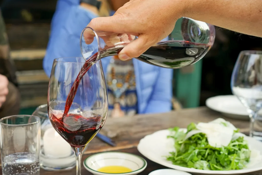 Red wine being poured into a glass beside a meal