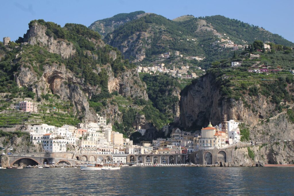 A coastal town on the Amalfi Coast beneath steep green cliffs, viewed from the water.
